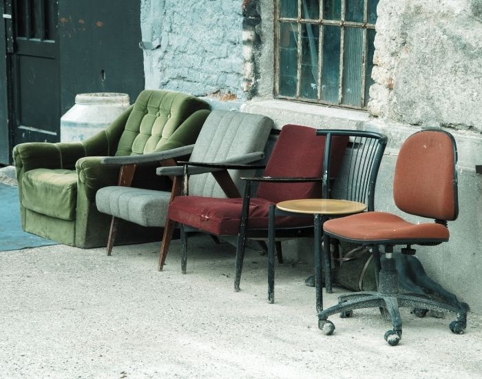 Five different chairs in different shapes, styles and colours lined up in front of a rustic building front.