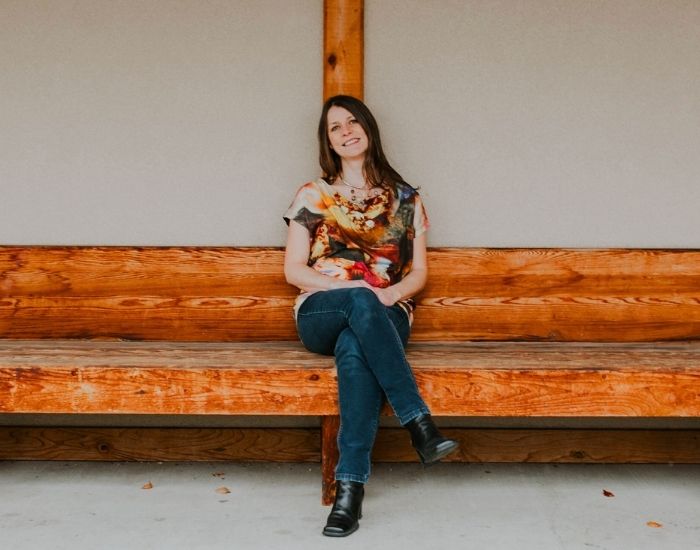 A dark haired woman sitting on a long wooden bench.