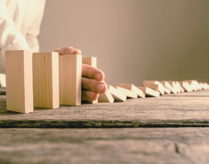 Someone's arm stopping the fall over of a row of wooden block dominoes.