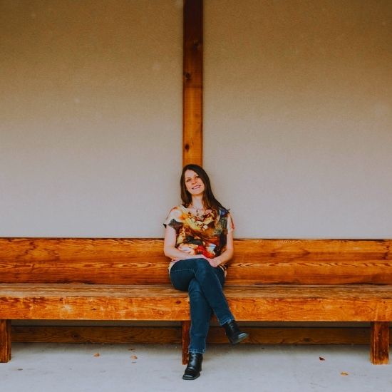 A dark haired woman sitting on a long wooden bench.